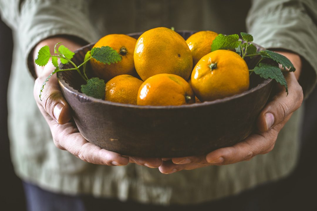 Manos sostienen un cuenco con mandarinas y naranjas, de Frutas Benito en Vigo.