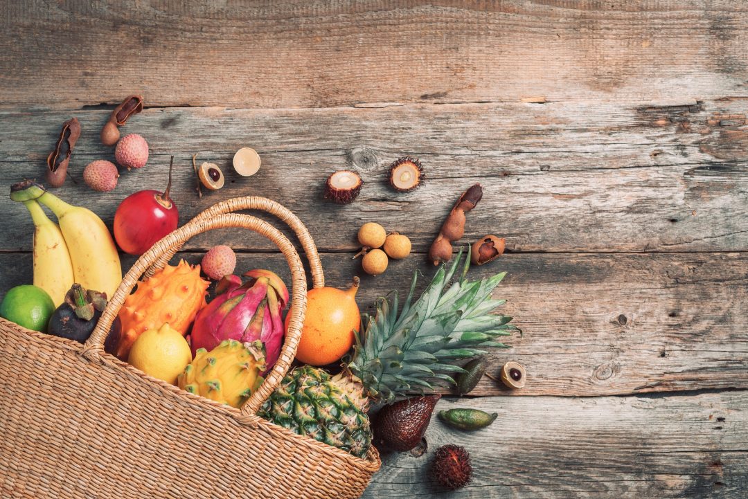 Superficie de madera con una cesta de mimbre llena de frutas y verduras de Frutas Benito en Vigo.